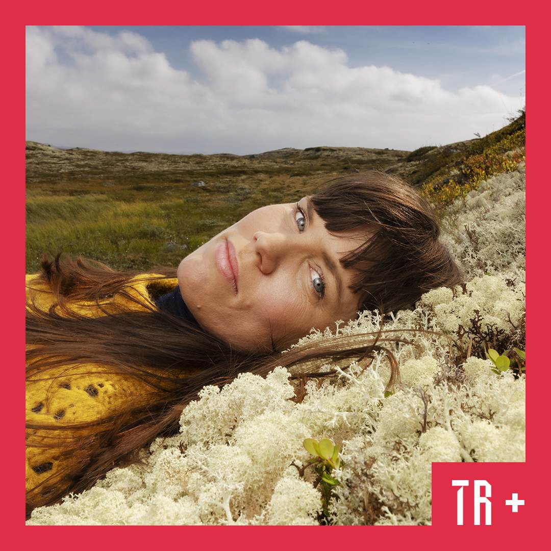 Photo: Agnete Brun A woman with long dark hair lays on a bed of foliage. She looks directly to camera.