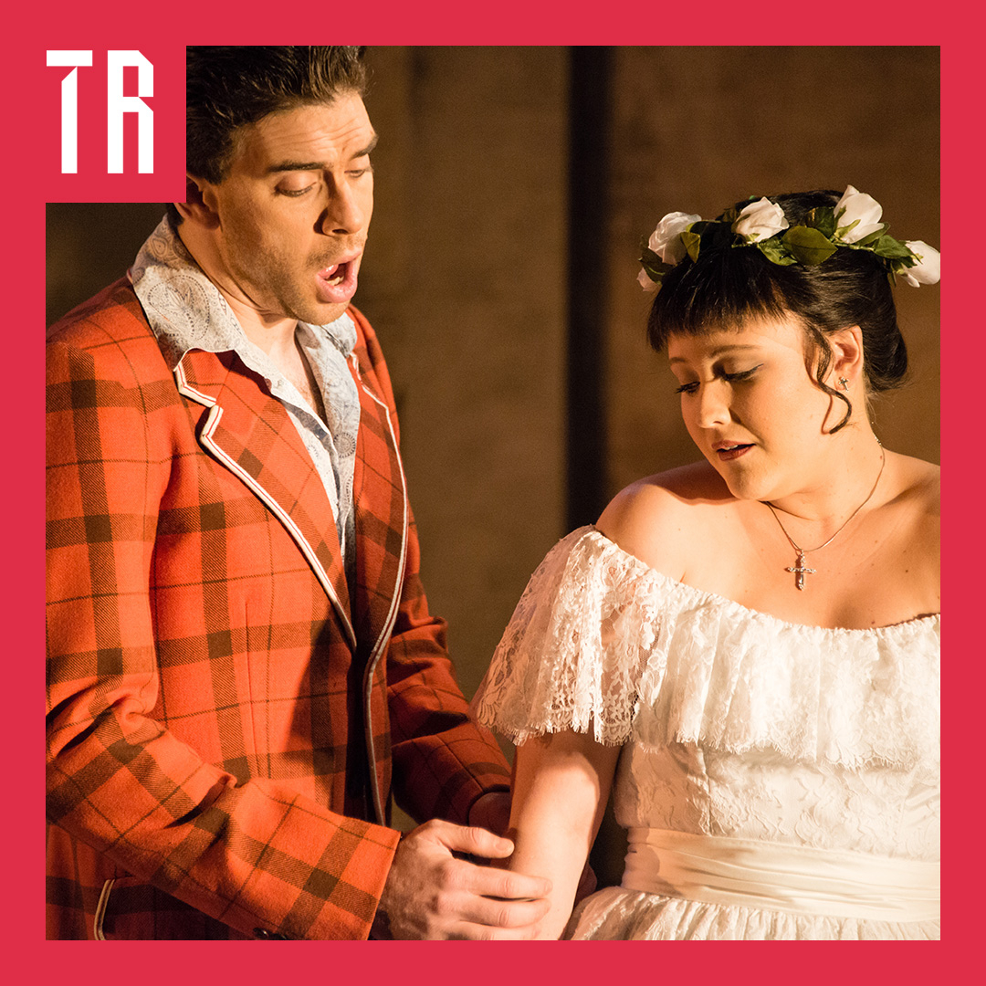 Photo: Albert Comper A man waering a red tweed coast sings to a woman in a white lace off the sholder dress with white roses in her hair