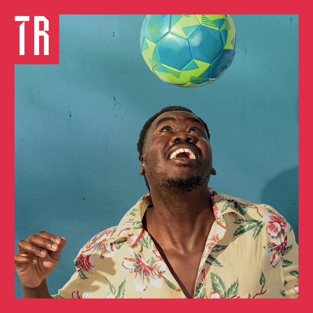 Photo: Daniel Boud An African man wearing a tropical shirt smile as he looks at a soccer ball suspended mid air