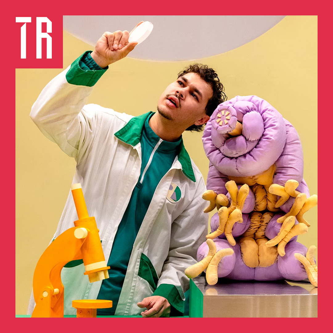 Image: supplied An actor dressed as a scientist is holding a pietrie dish up to the light, next to him a puppet tardigade, the size of a dog, looks on