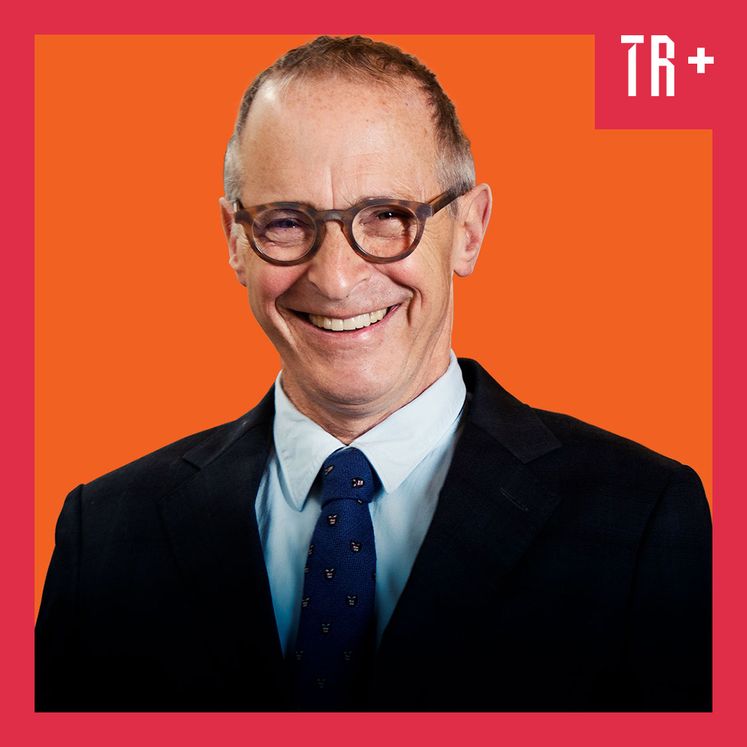 Image: Anne Fishbein A portrait of writer and humorist David Sedaris standing in a library, wearing a blazer and tie, holding a pipe